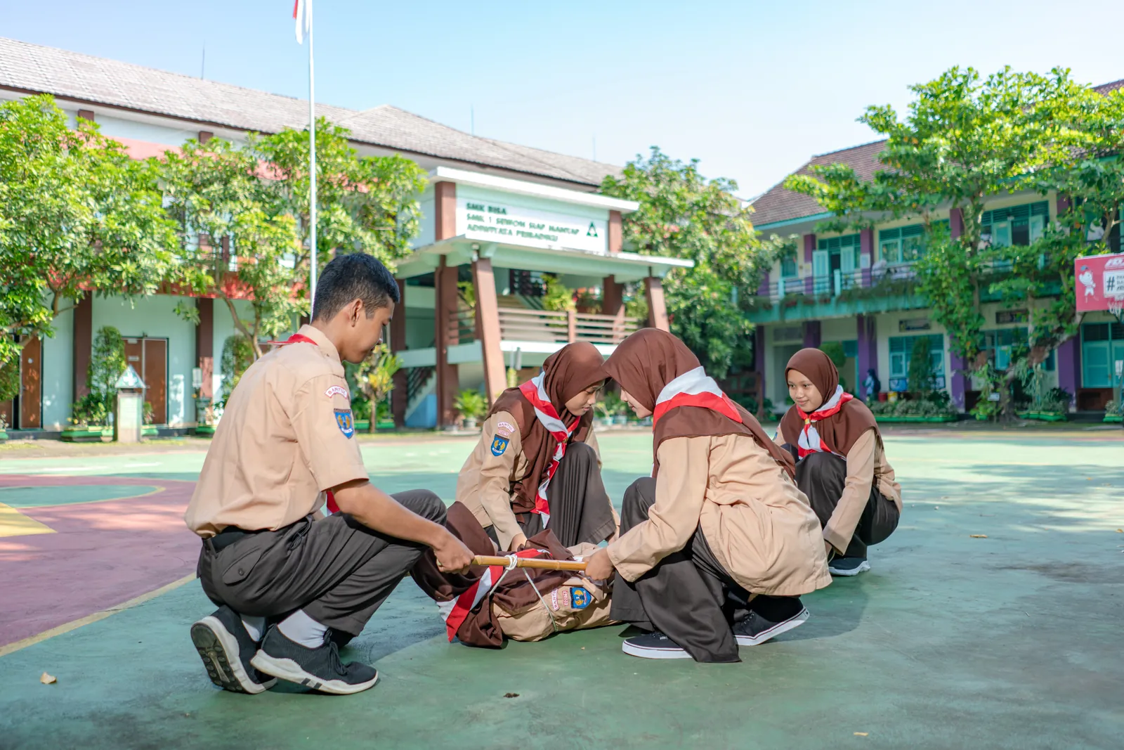 Anggota Pramuka berseragam coklat berlatih pertolongan pertama di halaman sekolah
